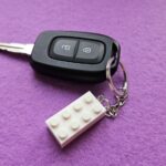 Autoschlüssel mit weißem Lego-Anhänger vor lila Hintergrund