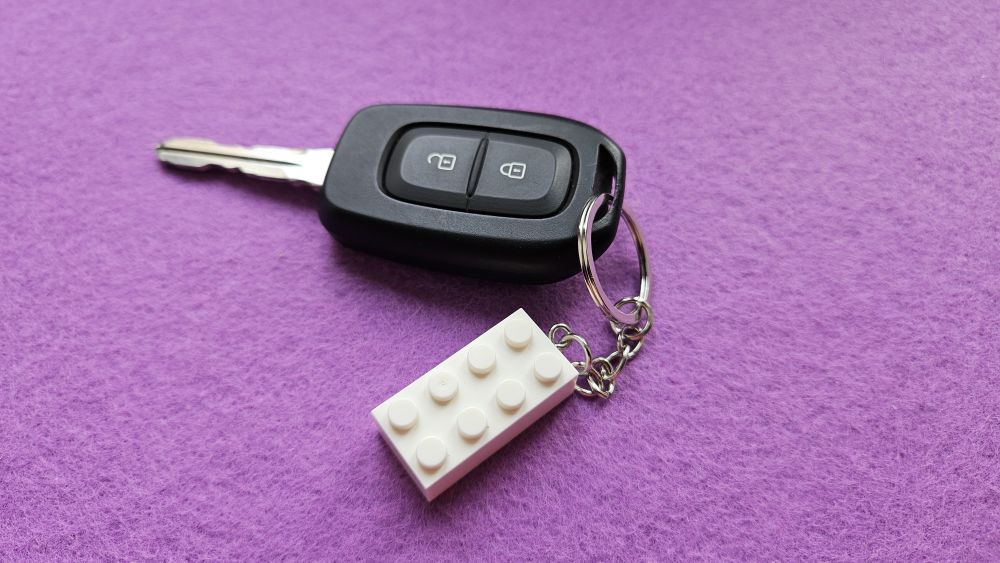 Autoschlüssel mit weißem Lego-Anhänger vor lila Hintergrund